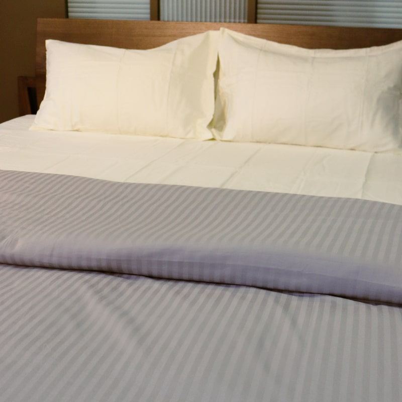 Placed on a bed, the Moon White Classic Solid Bedsheet, a cream king size and queen size cotton bedsheet you can buy online at Sukham Home, a sustainable furniture, gardening and home decor store in Kolkata, India