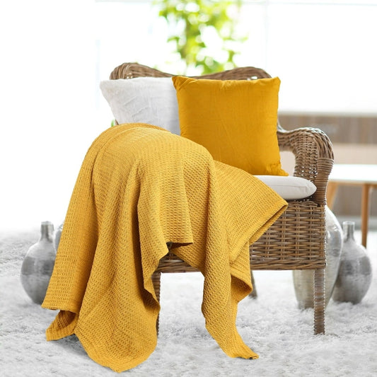 Placed on a chair, the Mustard Waffle Cotton Throw with Cushion Cover, a yellow throw and cover set you can buy online at Sukham Home, a sustainable furniture, kitchen & dining and home decor store in Kolkata, India