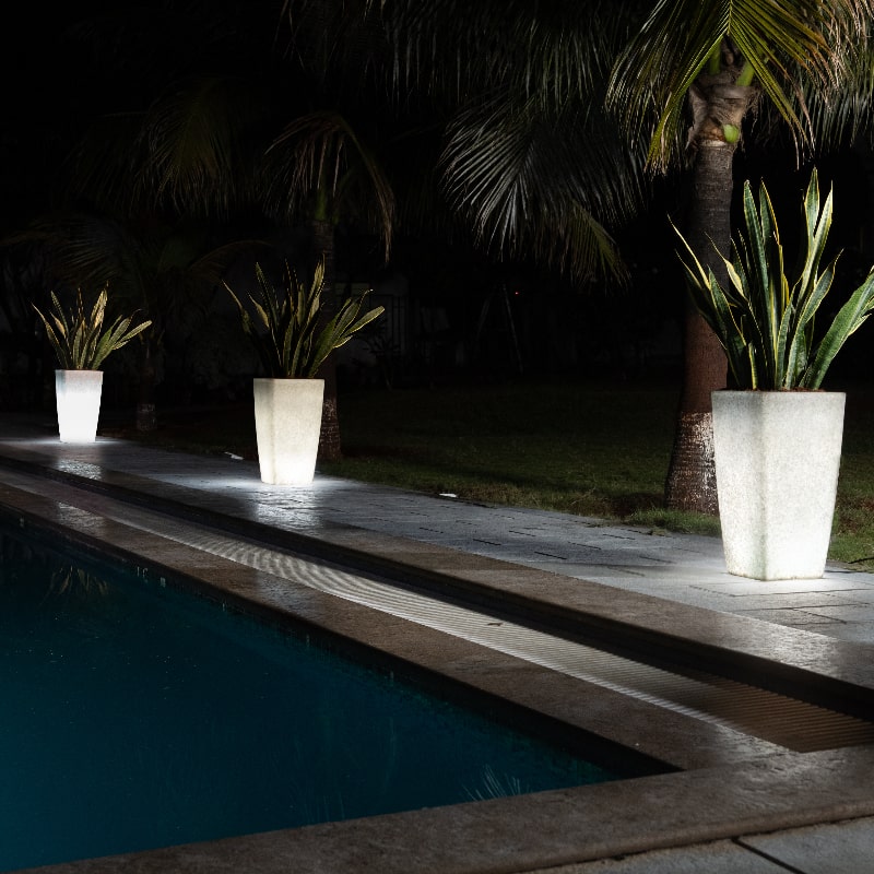 Arranged by the swimming pool, three Paris, a tall square stone finish plastic planter that looks like granite and comes with LED lights available at Sukham Home, a sustainable furniture, gardening and home decor store in Kolkata, India