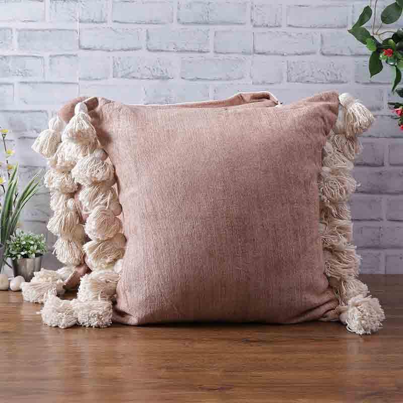 On a wooden floor, the Pinky Winky Cushions, a set of two pink velvet accent pillows with tassels you can buy online at Sukham Home, a sustainable furniture, kitchen & dining and home decor store in Kolkata, India