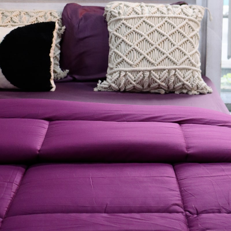 Placed on a bed with the Plum Bedsheet, Plum Solid Comforter, a purple king size cotton bedsheet you can buy online at Sukham Home, a sustainable furniture, gardening and home decor store in Kolkata, India