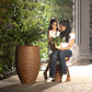 Placed outdoors, the Rustic Brown Dual Tone Wood Rib High, a round tall textured luxury planter made from FRP you can buy online at Sukham Home, a sustainable furniture, gardening and home decor store in Kolkata, India