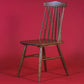Against a red background, the Oak Natural String Chair, a solid wood Windsor dining seat you can buy online at Sukham Home, a sustainable furniture and home decor store in Kolkata, India