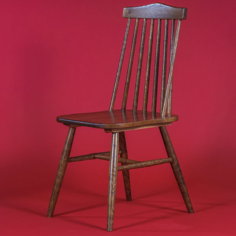 Against a red background, the Oak Natural String Chair, a solid wood Windsor dining seat you can buy online at Sukham Home, a sustainable furniture and home decor store in Kolkata, India