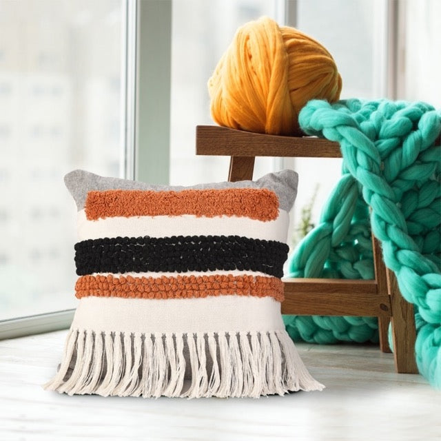 Placed on the floor, the Tasselled & Tufted Cushion, a square white and orange accent pillow available at Sukham Home, a sustainable furniture, kitchen & dining and home decor store in Kolkata, India