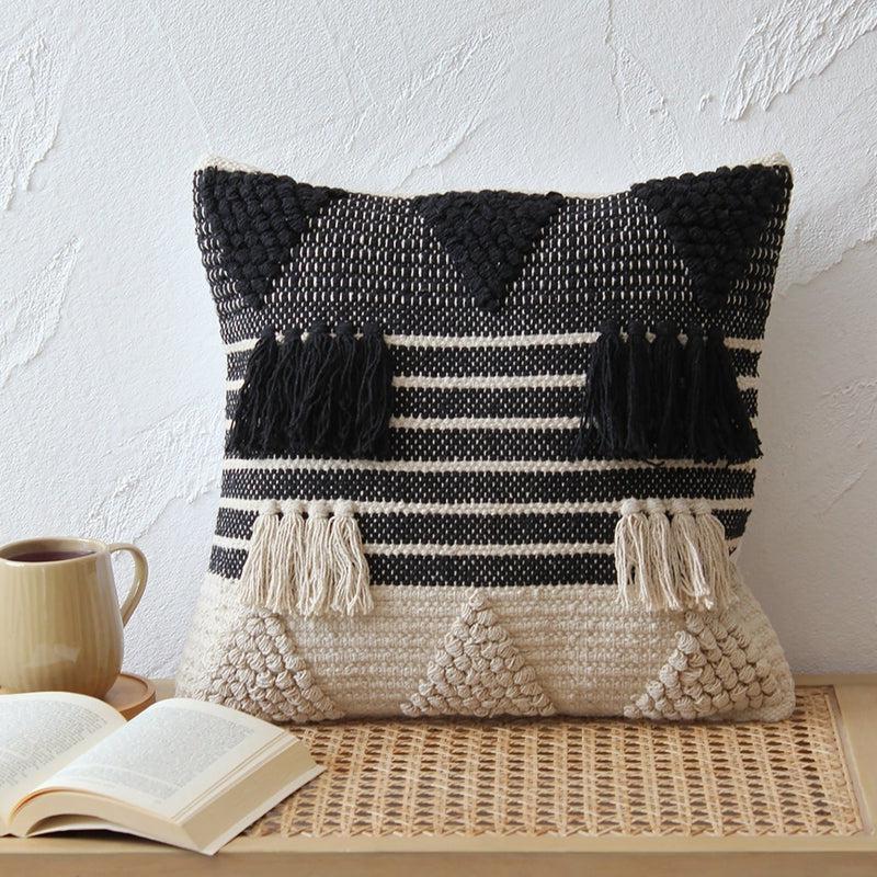 Against a white wall on a table, the Tassels & Triangles Cushion, a black and white tufted accent pillow you can buy online at Sukham Home, a sustainable furniture, kitchen & dining and home decor store in Kolkata, India