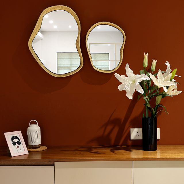 Placed on a red wall, the Twist Mirror, a mirror frame made from golden grass that you can buy online at Sukham Home, a sustainable furniture, kitchen & dining and home decor store in Kolkata, India