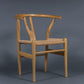 Against a grey background, the Oak Natural Wishbone Chair, a solid wood rattan dining seat you can buy online at Sukham Home, a sustainable furniture and home decor store in Kolkata, India