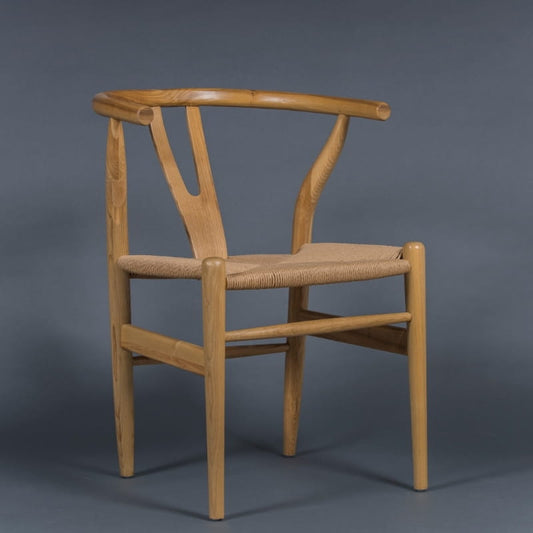 Against a grey background, the Oak Natural Wishbone Chair, a solid wood rattan dining seat you can buy online at Sukham Home, a sustainable furniture and home decor store in Kolkata, India