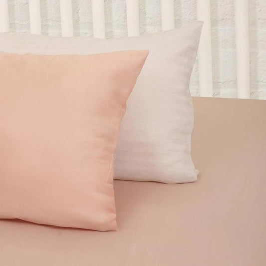 Against a white pillow, the Pink Solid Bedsheet, a pale pink king and queen size cotton bedsheet you can buy online at Sukham Home, a sustainable furniture, gardening and home decor store in Kolkata, India