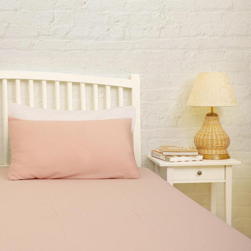 Arranged on a bed, the Pink Solid Bedsheet, a pale pink king and queen size cotton bedsheet you can buy online at Sukham Home, a sustainable furniture, gardening and home decor store in Kolkata, India