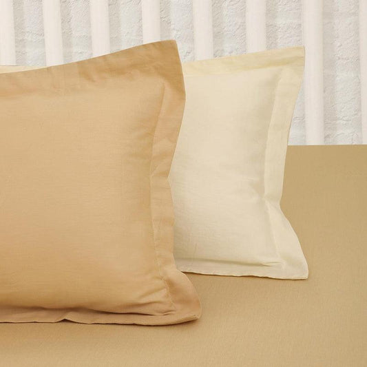 Placed against a white pillow, the pillowcase of the Mustard Solid Bedsheet, a yellow ochre king and queen size cotton bedsheet you can buy online at Sukham Home, a sustainable furniture, gardening and home decor store in Kolkata, India