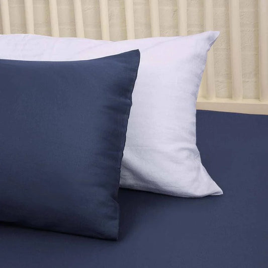 A white pillow and the navy blue pillow from the Navy Blue Classic Solid Bedsheet, a king size and queen size cotton bedsheet you can buy online at Sukham Home, a sustainable furniture, gardening and home decor store in Kolkata, India